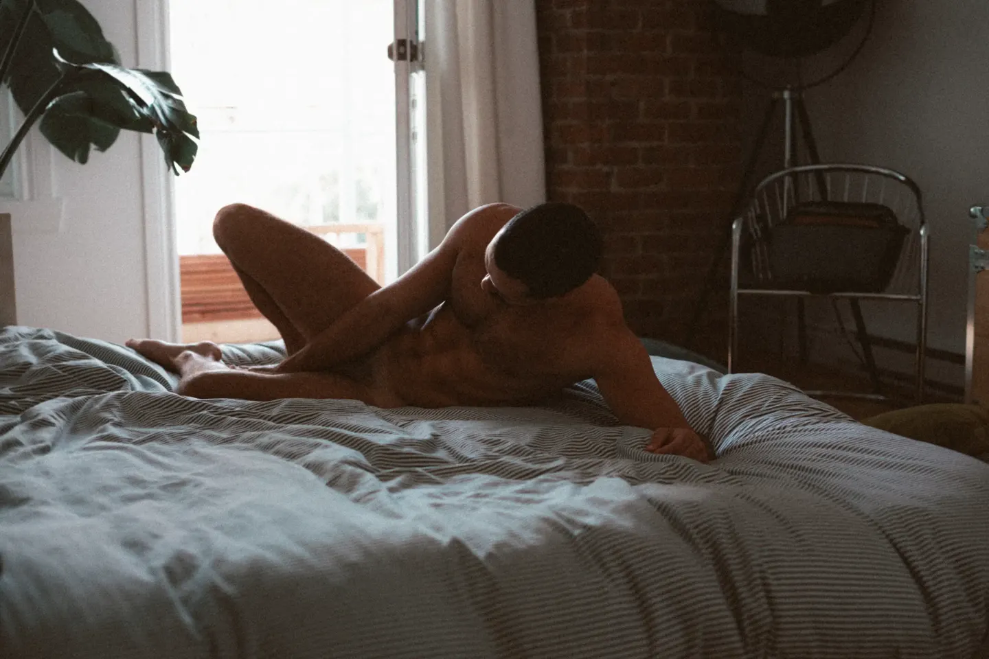 Portrait boudoir masculin allongé — nu intégral dos lumière naturelle